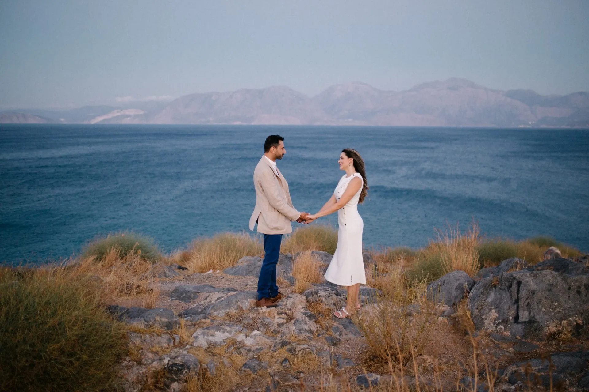 Couple holding hands on the rocky coast of Crete at dusk